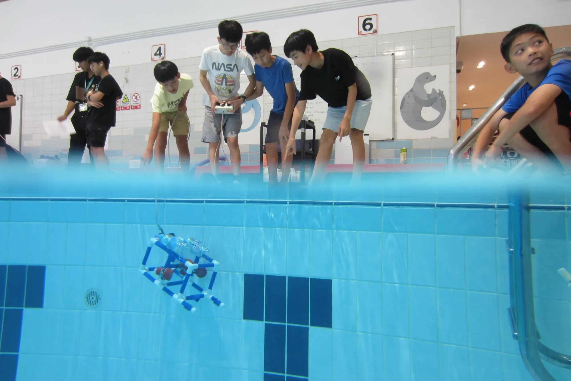Students controlling a small underwater robot from the edge of a swimming pool.